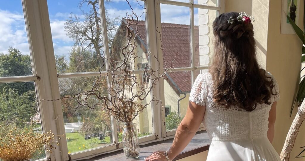 Braut sieht aus einem großen Fenster auf den Ort der Trauung